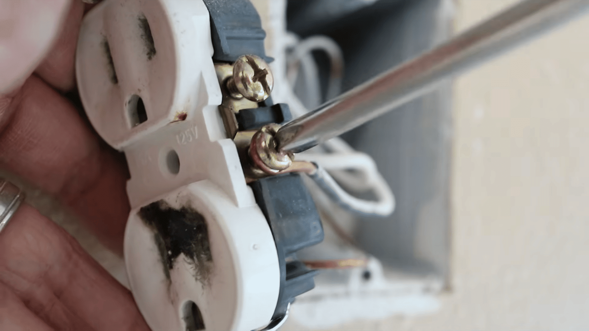 close up of screwdriver unscrewing golden bolt of a white outlet attached to a black wire