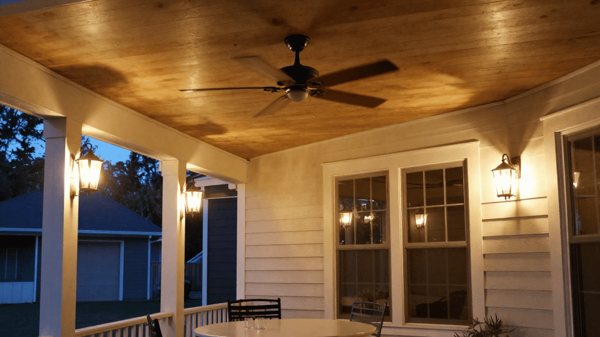 covered porch featuring a modern ceiling fan and warm hanging pendant lights at night