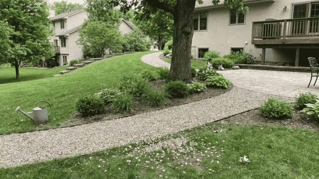 curved gravel path winding through a sloped backyard lawn toward the patio