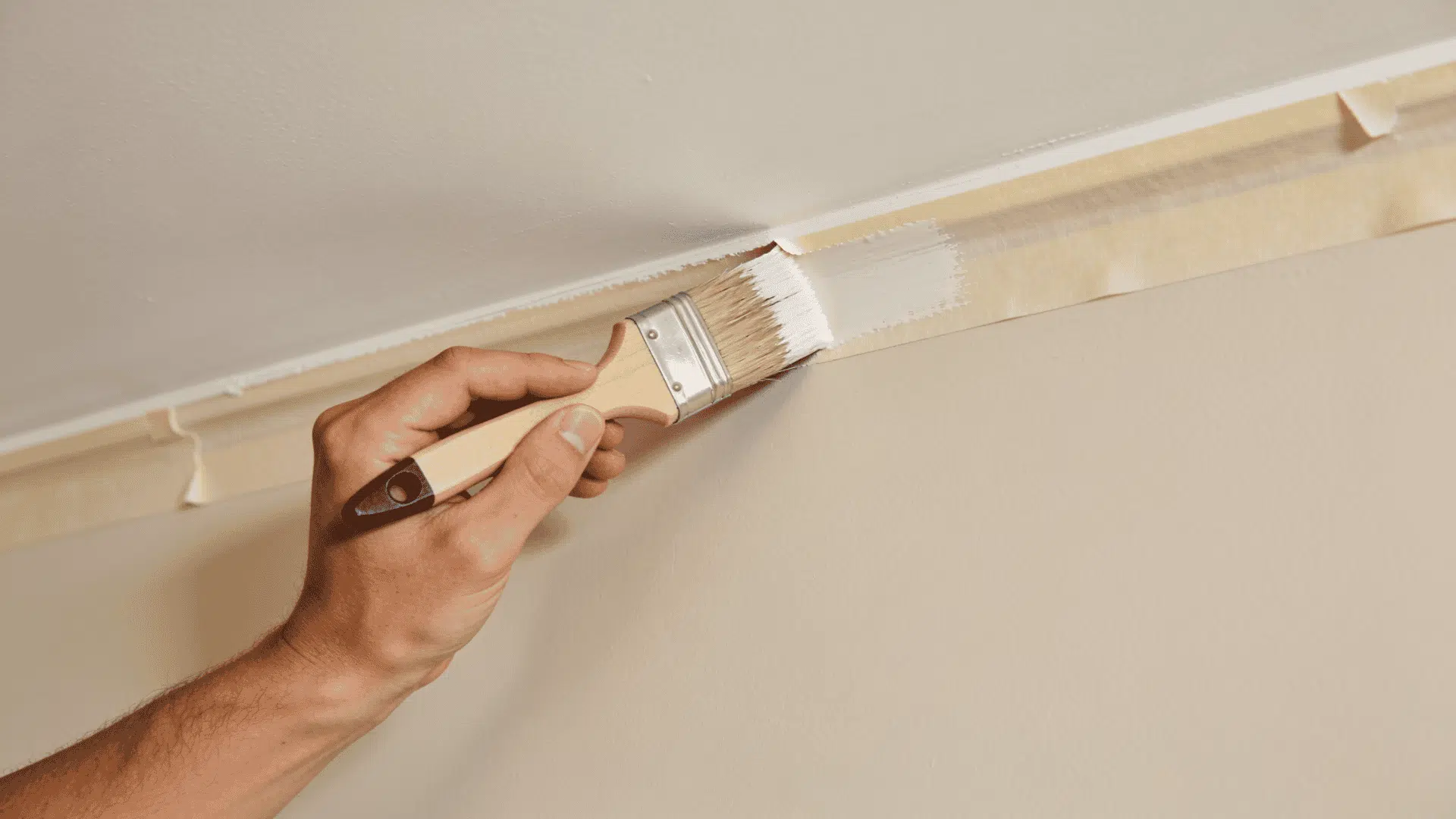 person cutting in around the ceiling edge with an angled brush for clean paint lines