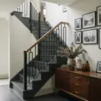 dark gray painted staircase with black metal railing gallery wall and wood sideboard in a modern entryway