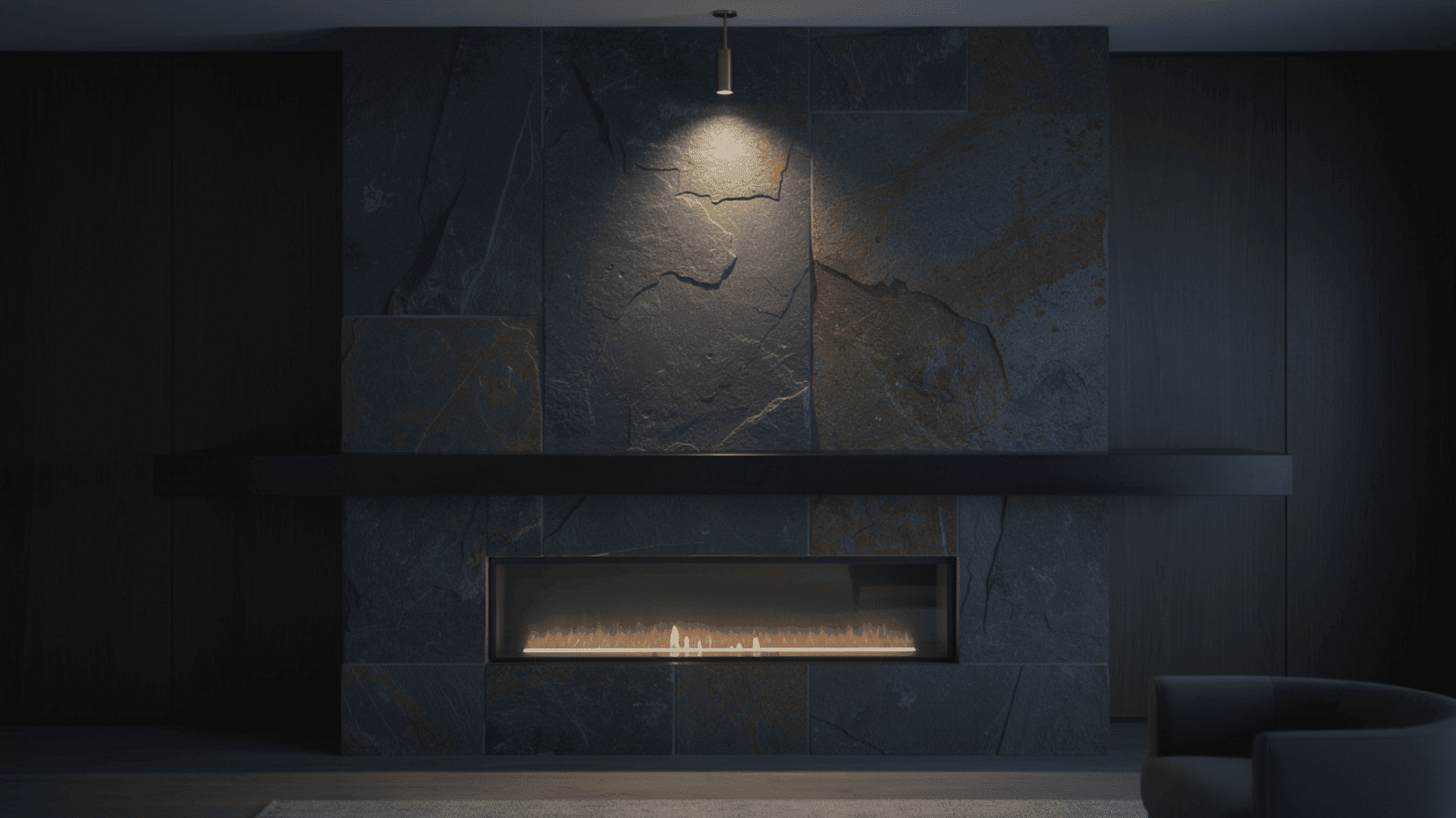 dark slate fireplace wall with large format cleft slate tiles in charcoal blue and rust tones housing a recessed linear gas burner lit from above by a single pendant spotlight in a moody dark room
