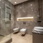 Modern bathroom with marble walls, glass shower door, wall-mounted toilet, and sleek white sink