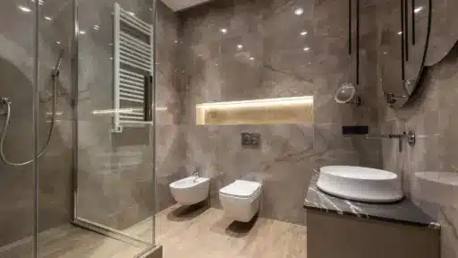 Modern bathroom with marble walls, glass shower door, wall-mounted toilet, and sleek white sink