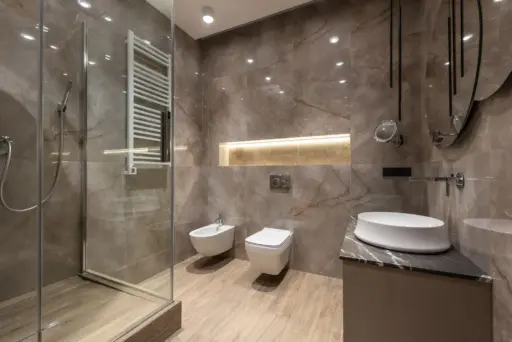 Modern bathroom with marble walls, glass shower door, wall-mounted toilet, and sleek white sink