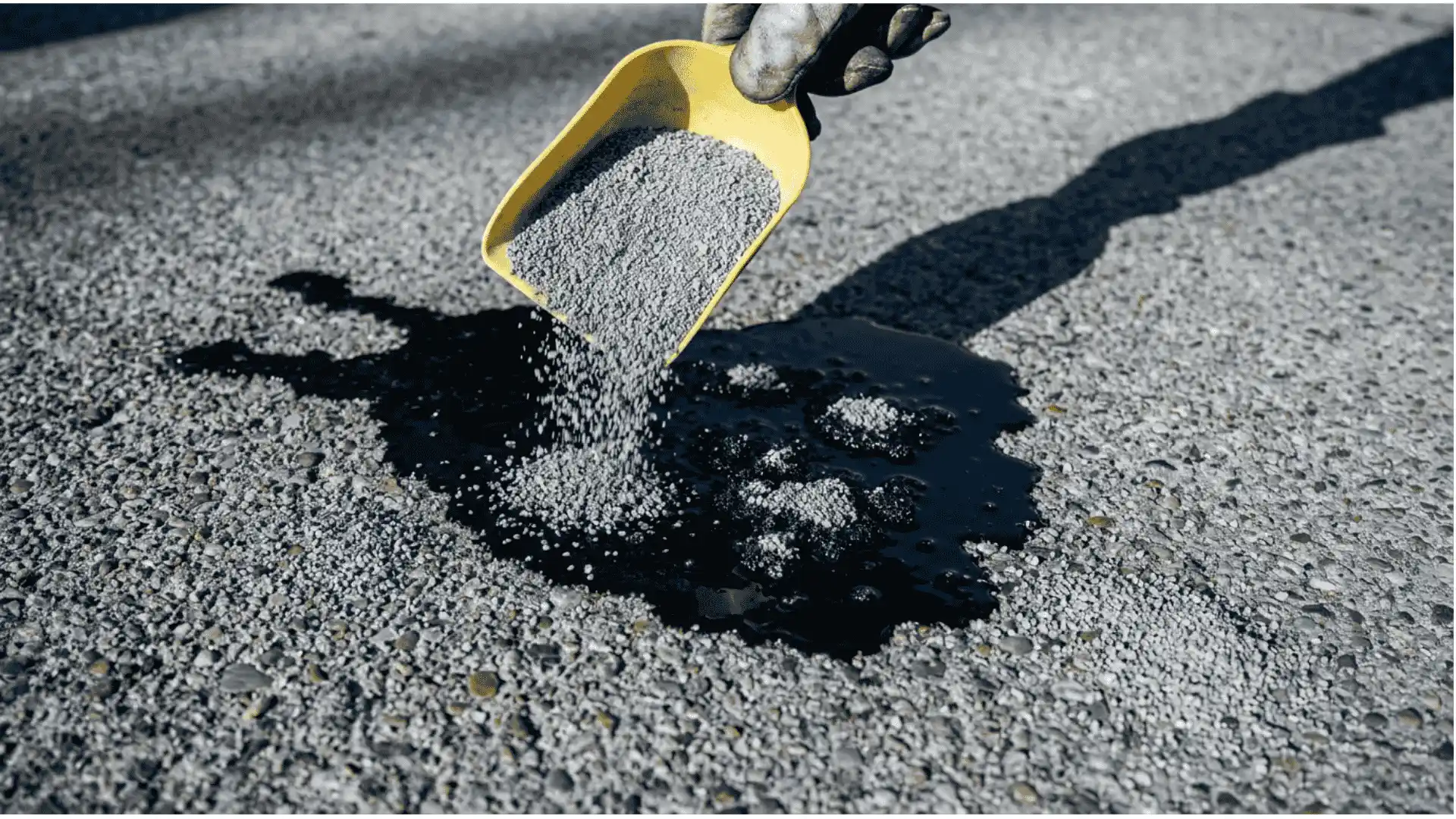 hand pouring non clumping cat litter onto a fresh dark oil spill on a concrete driveway