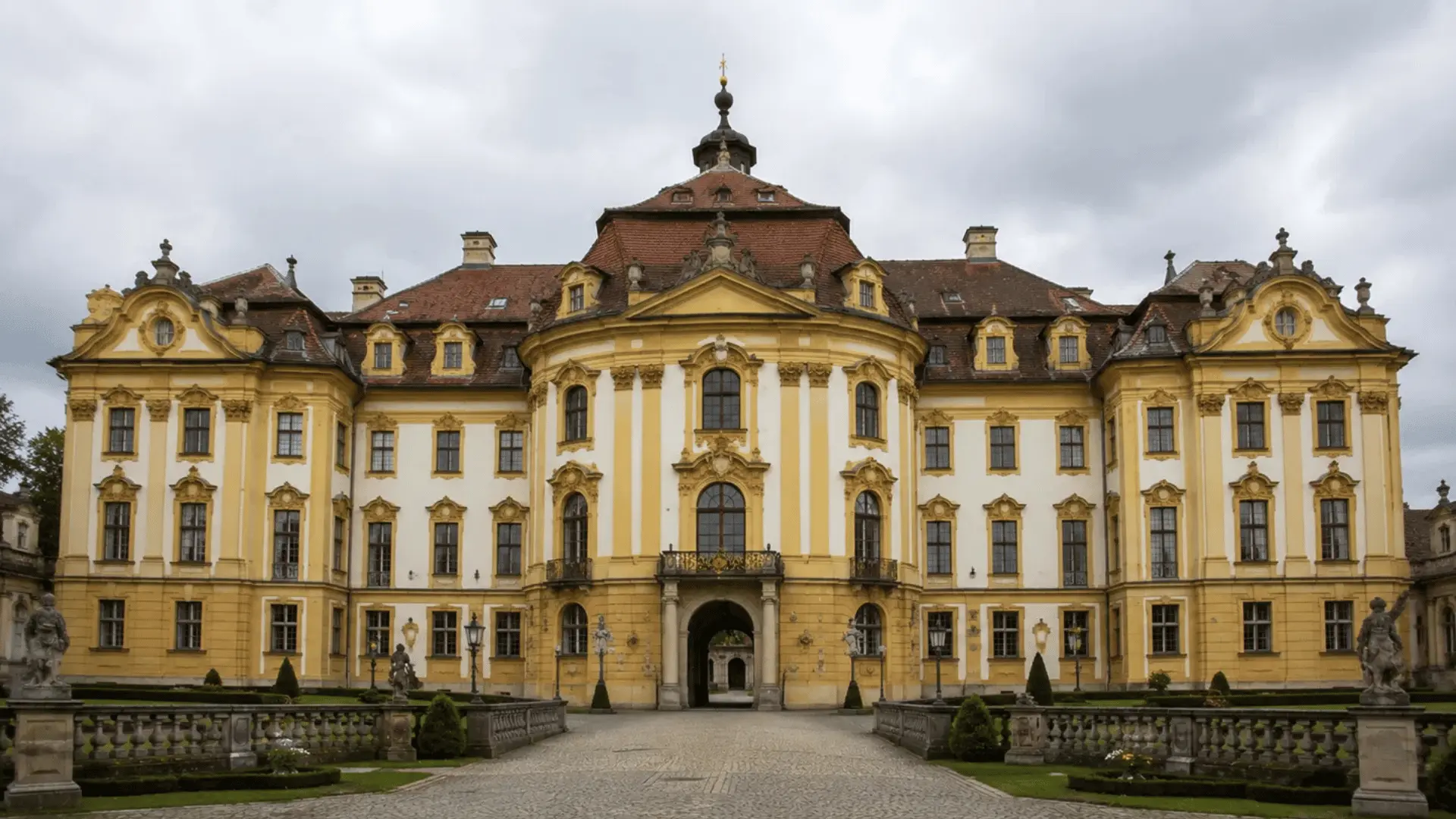 baroque yellow and white palace with curved central pavilion statues and a formal courtyard approach