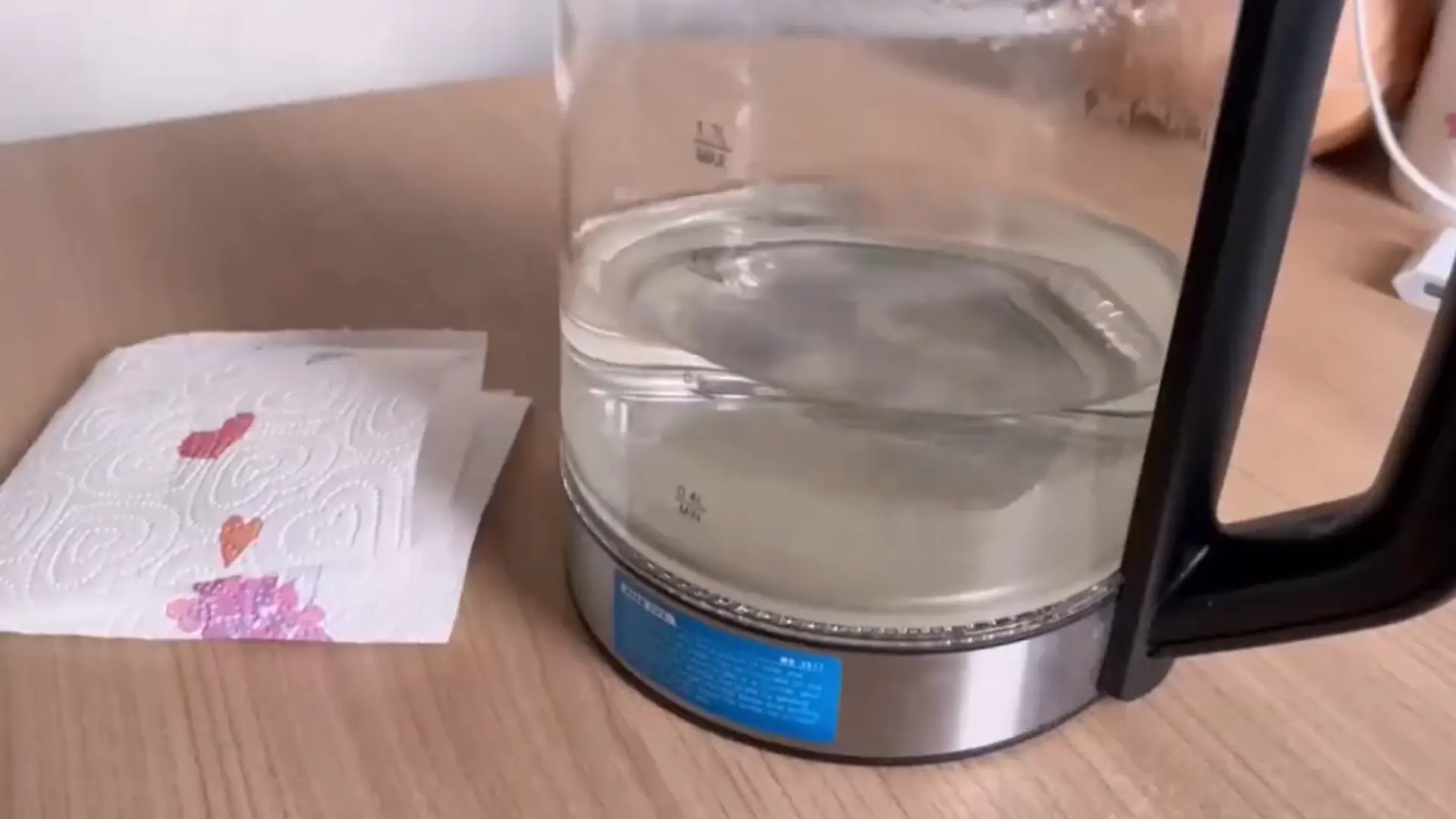 glass kettle filled with hot water next to stained paper towels on a light wooden tabletop