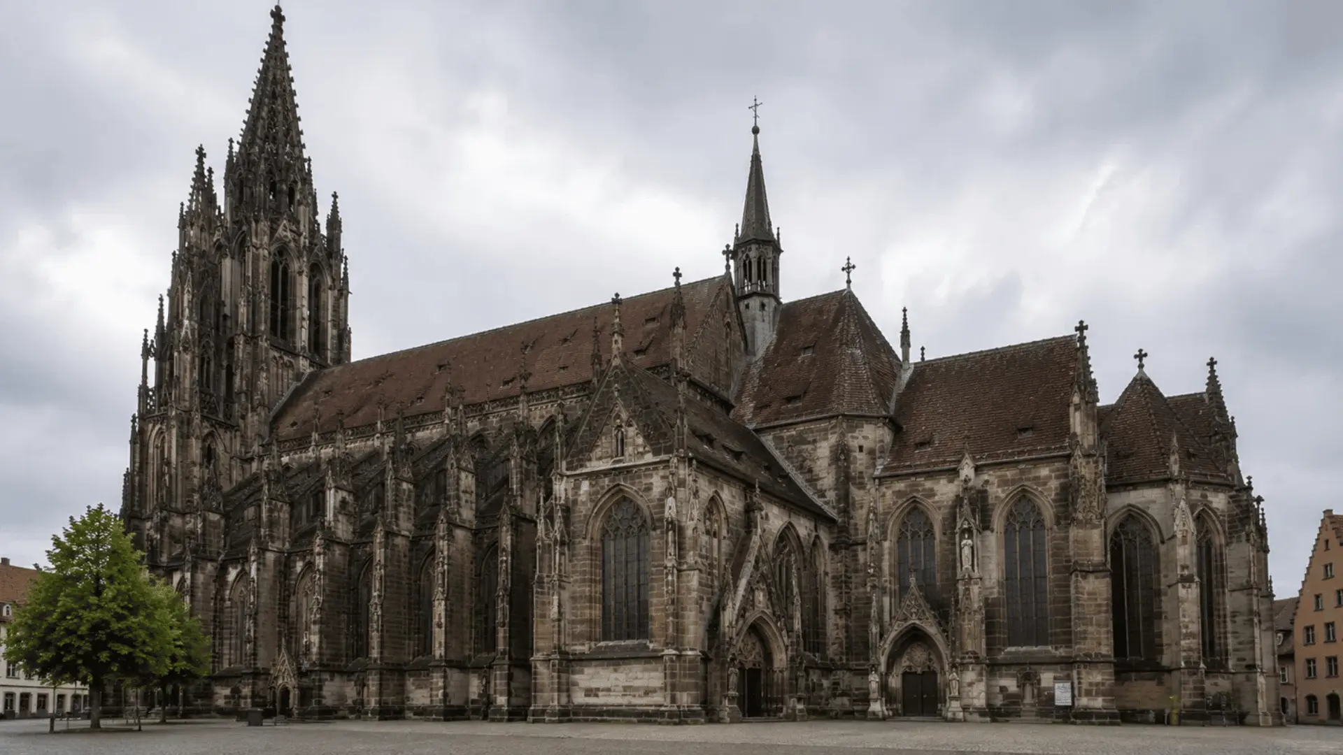 gothic cathedral with tall openwork spire pointed arches and steep tiled roofs on a cloudy day