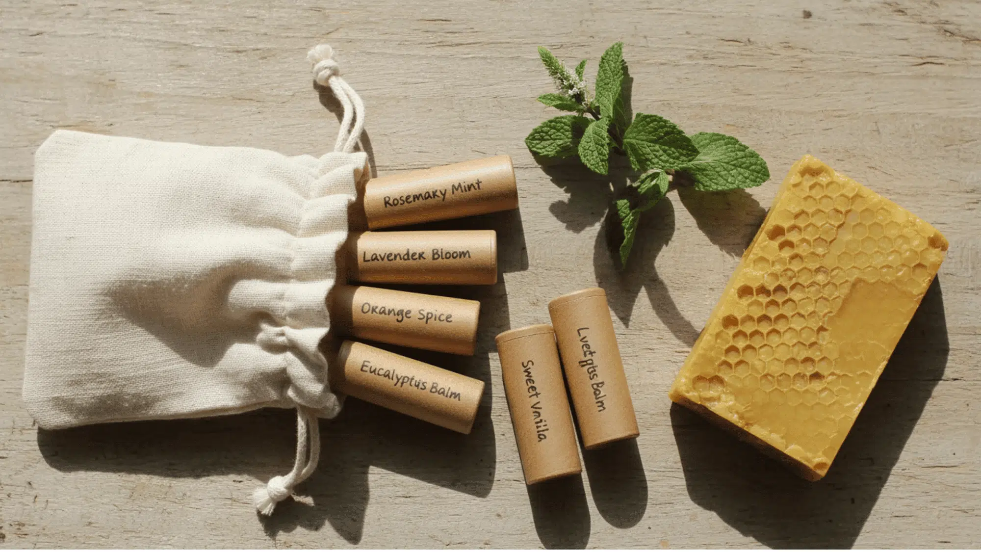 _handmade lip balm tubes spilling from a linen pouch beside mint and beeswax