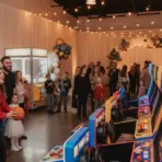 People enjoying arcade games at a lively indoor party with string lights and balloon decorations