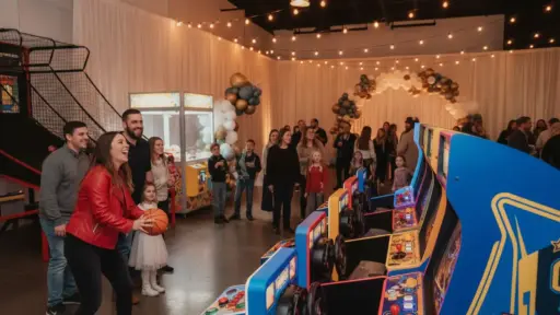 People enjoying arcade games at a lively indoor party with string lights and balloon decorations