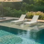 Two white lounge chairs by a luxurious pool with surrounding greenery