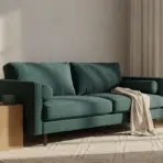 Teal sofa with knitted throw in sunlit living room beside wooden side table and modern lamp