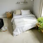 Cozy bedroom with neatly made bed, potted plants, and a fan on concrete floor