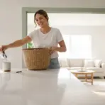 Woman placing paper in wicker basket on white countertop in bright living room