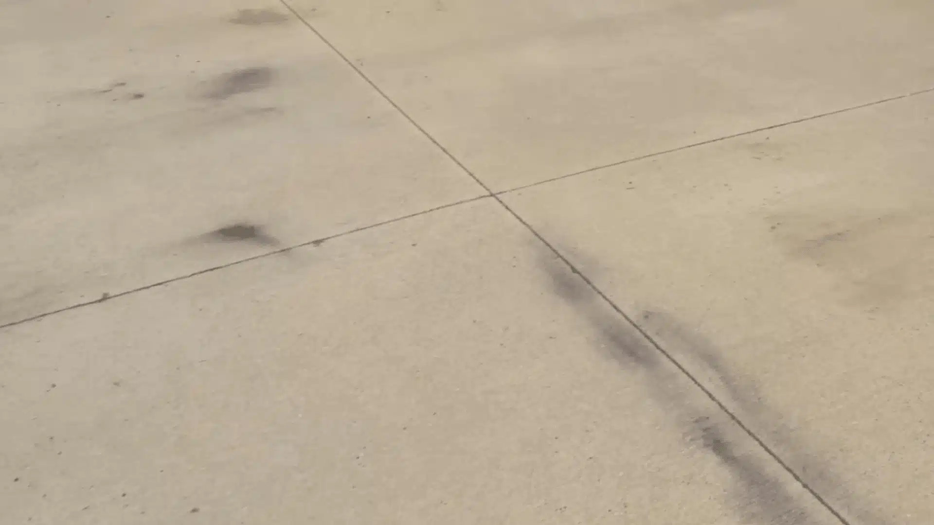 close up view of dark oil stains soaked into a concrete driveway surface near a crack