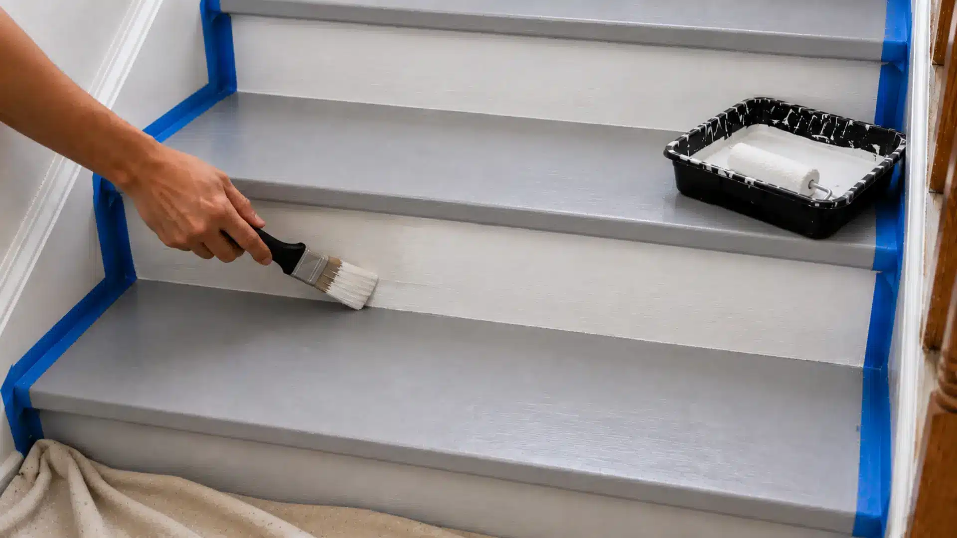 hand painting white stair risers while gray primed treads stay protected with tape