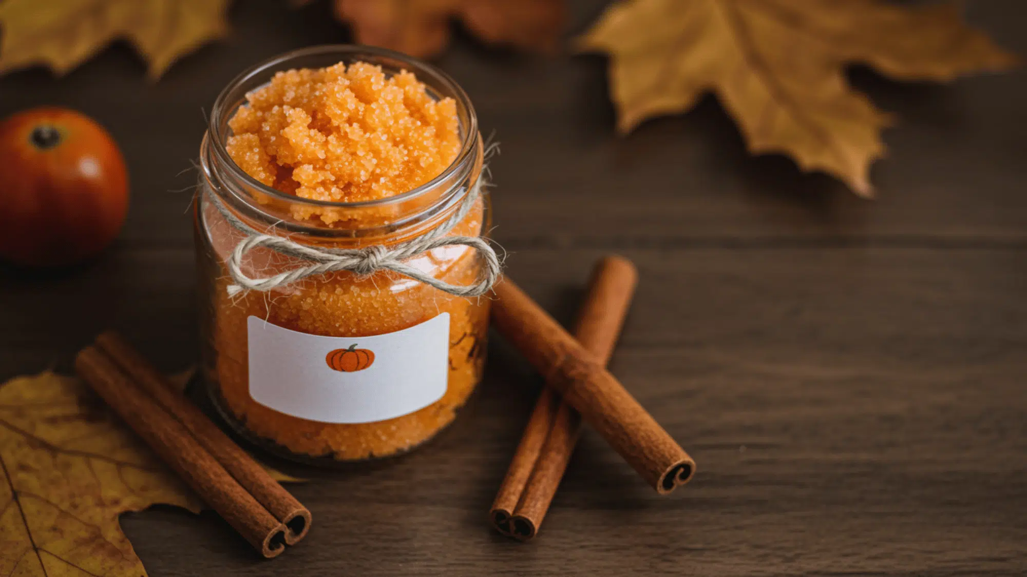 jar of pumpkin-colored sugar scrub with twine label and cinnamon stick on wood