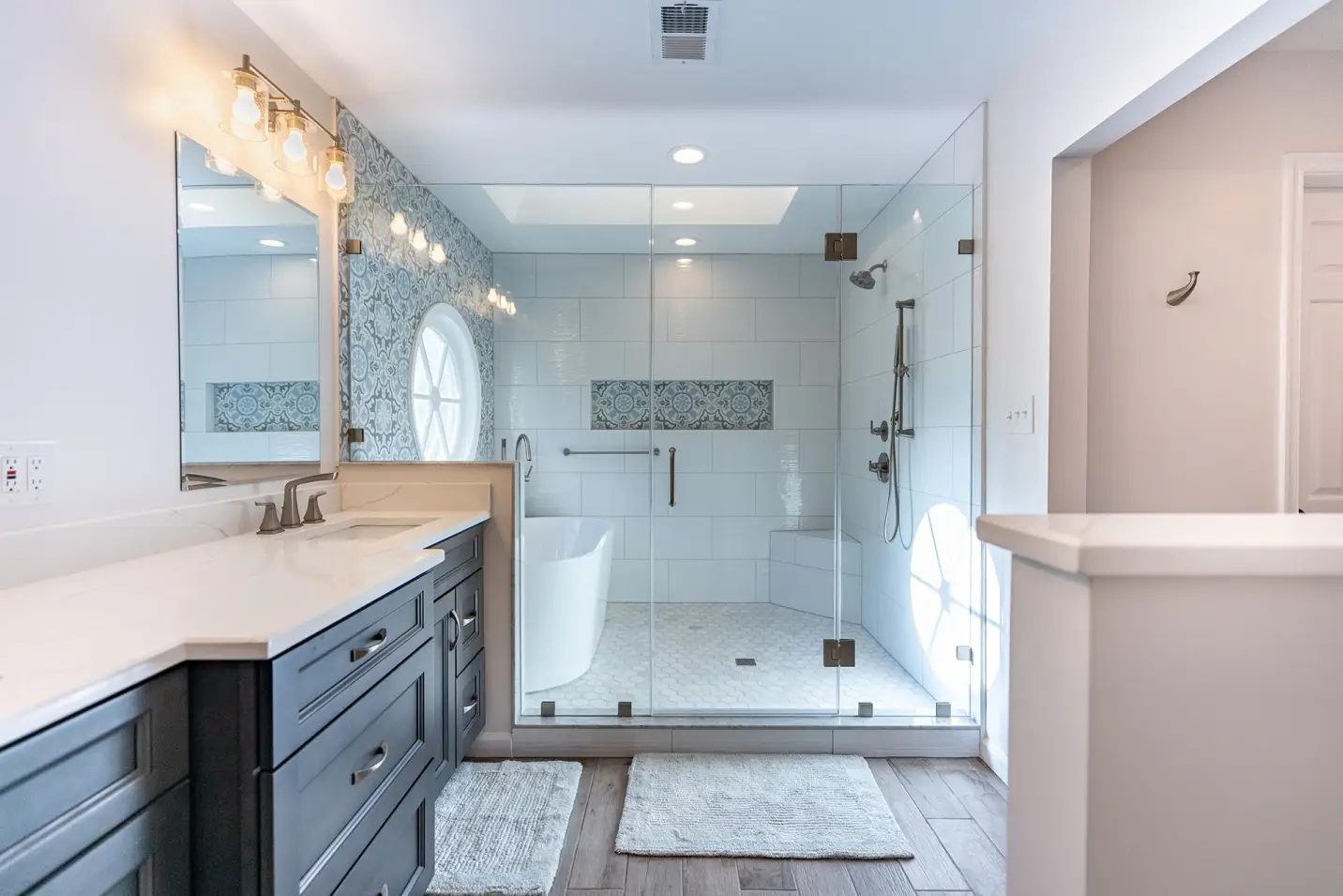 Modern bathroom with glass-enclosed shower, freestanding tub, and double vanity under warm lighting