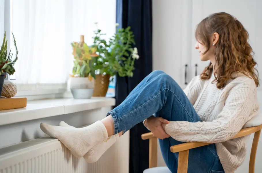 Woman in cozy sweater sitting on chair by window with indoor plants