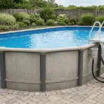 large above ground pool with ladder and filter system on a paved patio beside landscaped backyard gardens