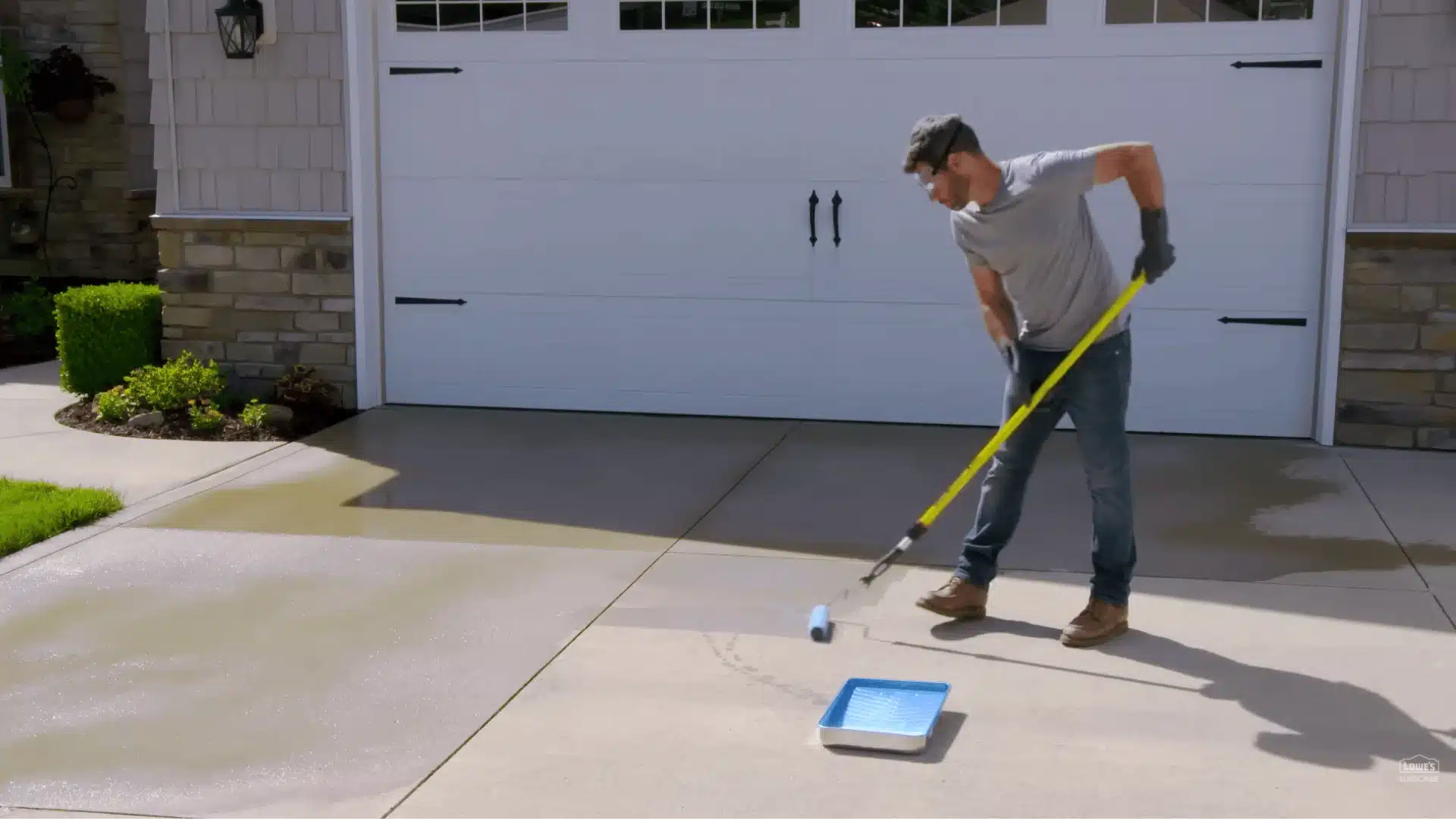 man rolling sealer onto a concrete driveway with a paint roller in front of a garage door