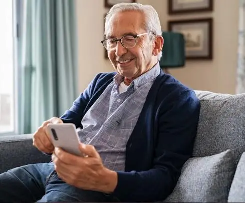 Elderly man using smartphone on gray sofa in cozy living room