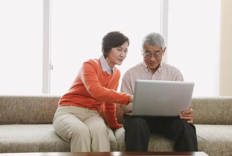 Elderly couple sitting on couch, using laptop together in a bright living room