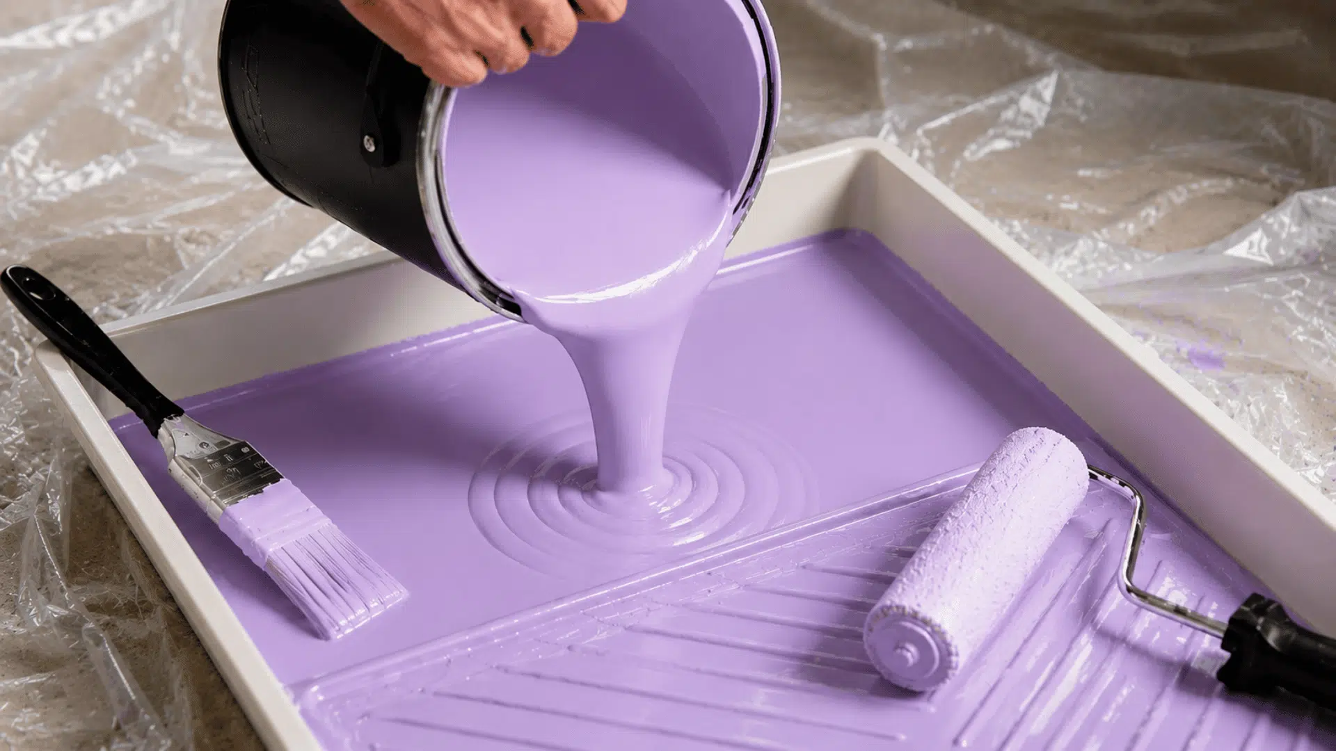 light purple enamel paint pouring into a tray with brush and roller on a protected work surface