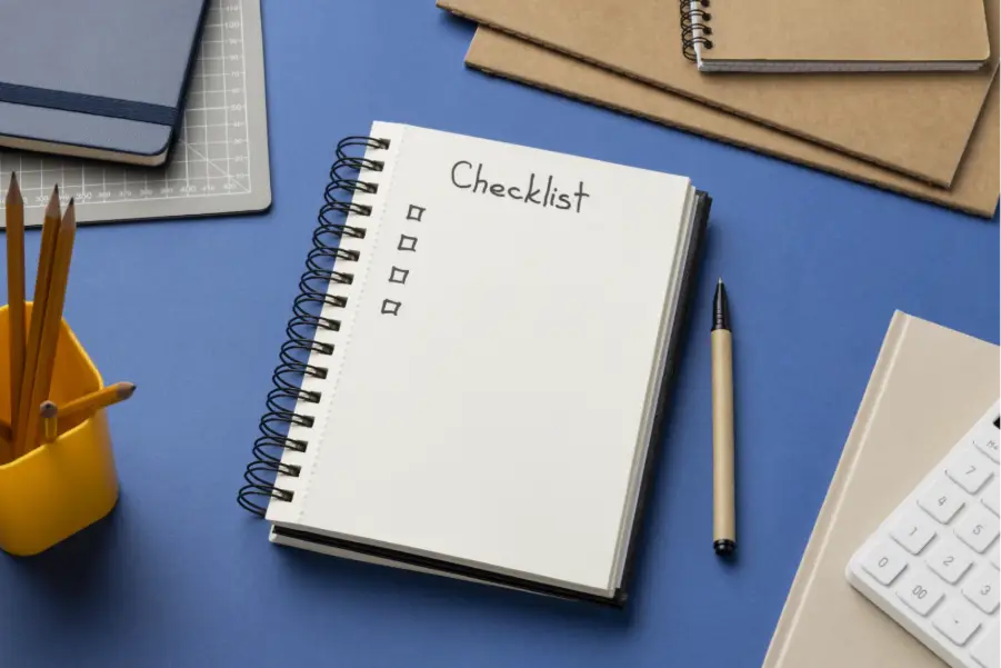 Spiral notebook with checklist on blue desk alongside pen and stationery items