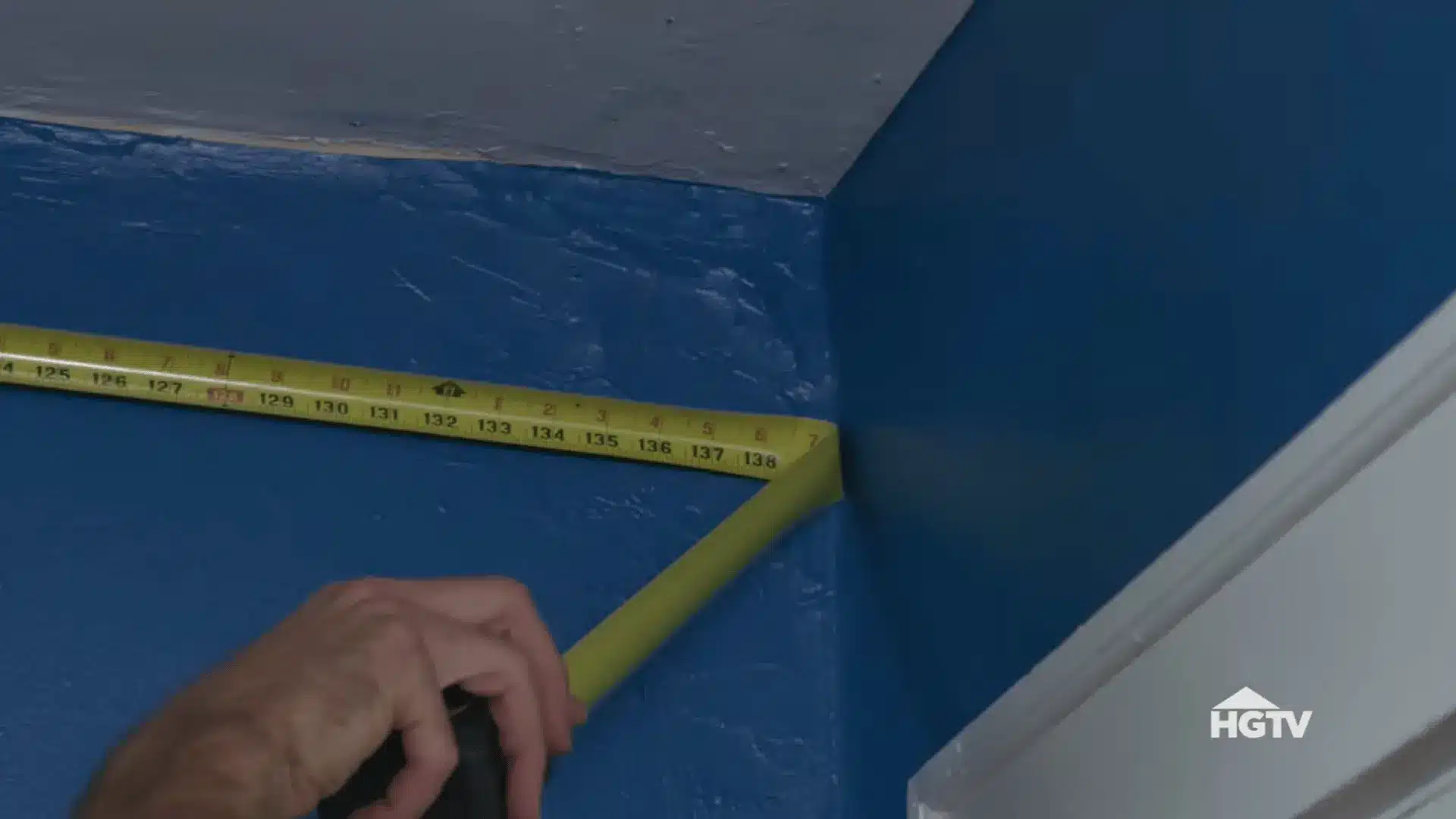 person measuring crown molding against wall and marking cut direction before making accurate miter saw cuts