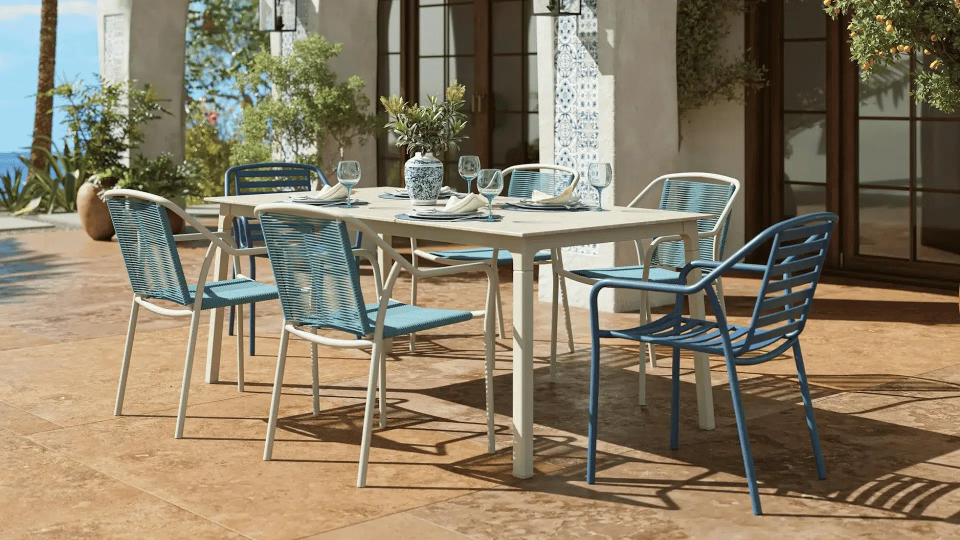 modern outdoor dining table with blue chairs arranged on sunny mediterranean style patio terrace