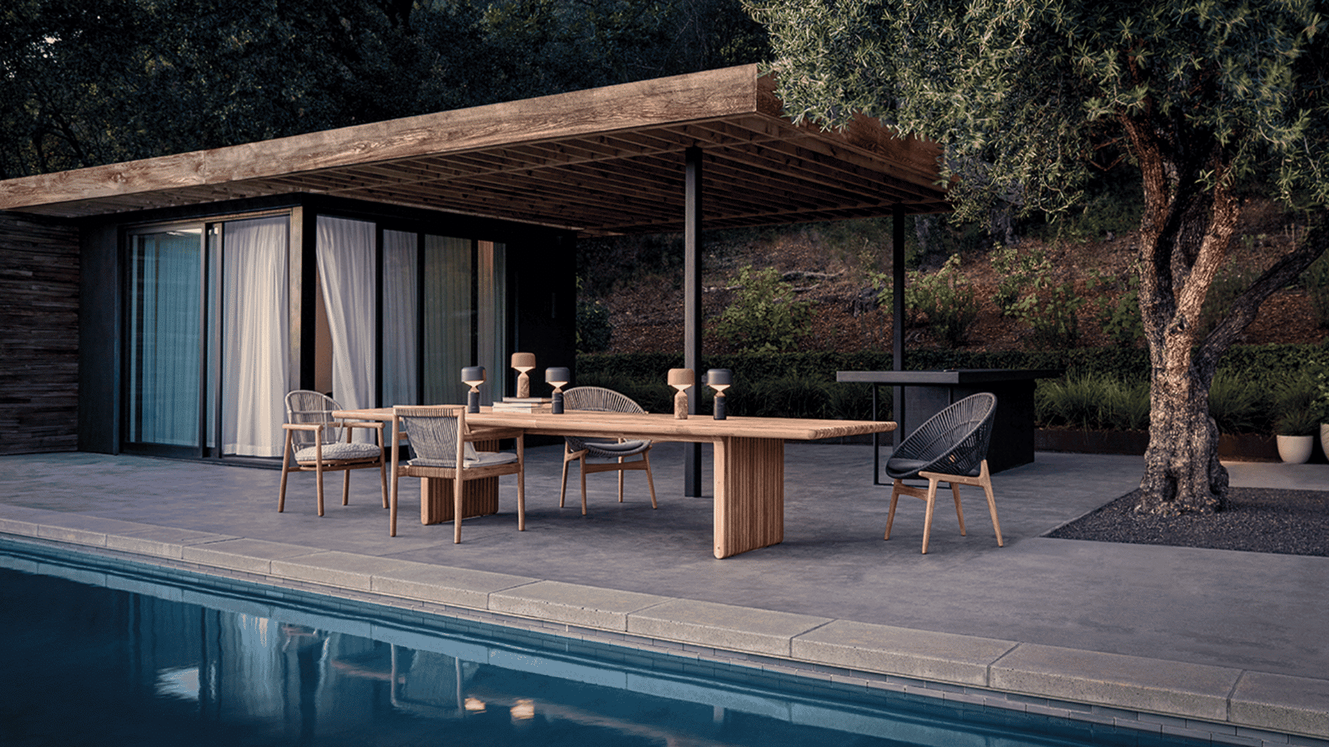 modern outdoor dining table with woven chairs beside pool under covered patio surrounded by trees