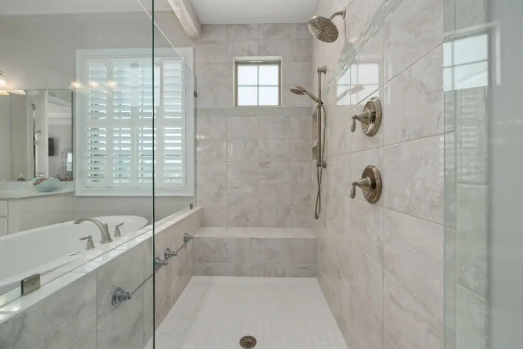 Modern bathroom with marble tiles, glass shower enclosure, and bathtub under natural light