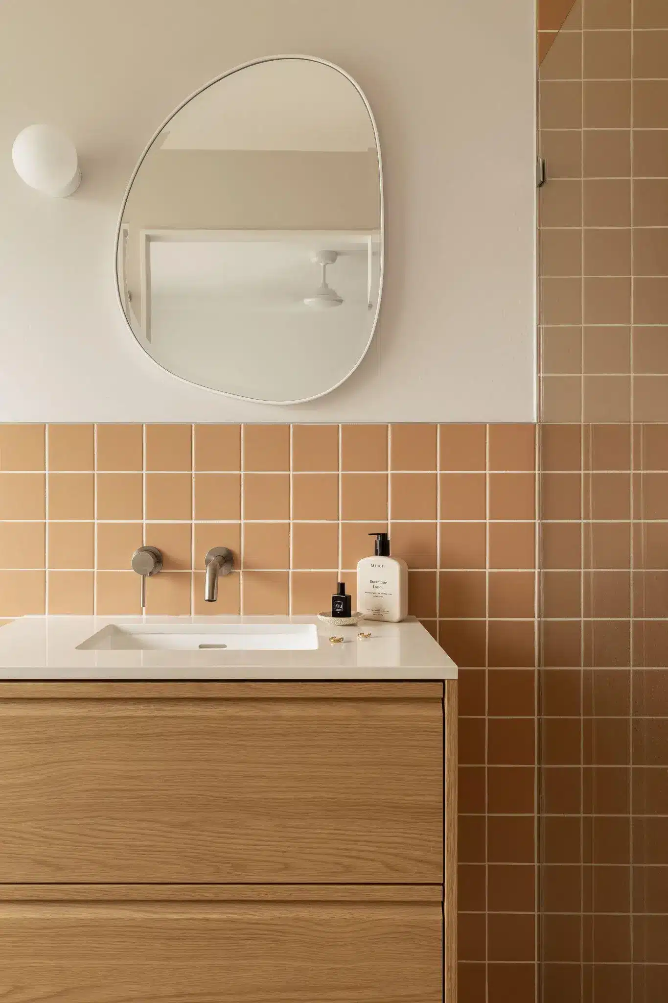 Modern bathroom vanity with terracotta tiles, large mirror, and minimalist soap dispensers
