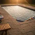 Outdoor swimming pool with wooden loungers and colorful floats at sunset