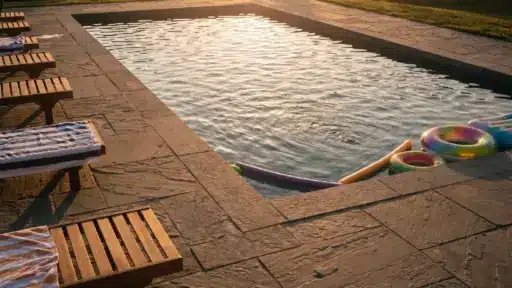 Outdoor swimming pool with wooden loungers and colorful floats at sunset