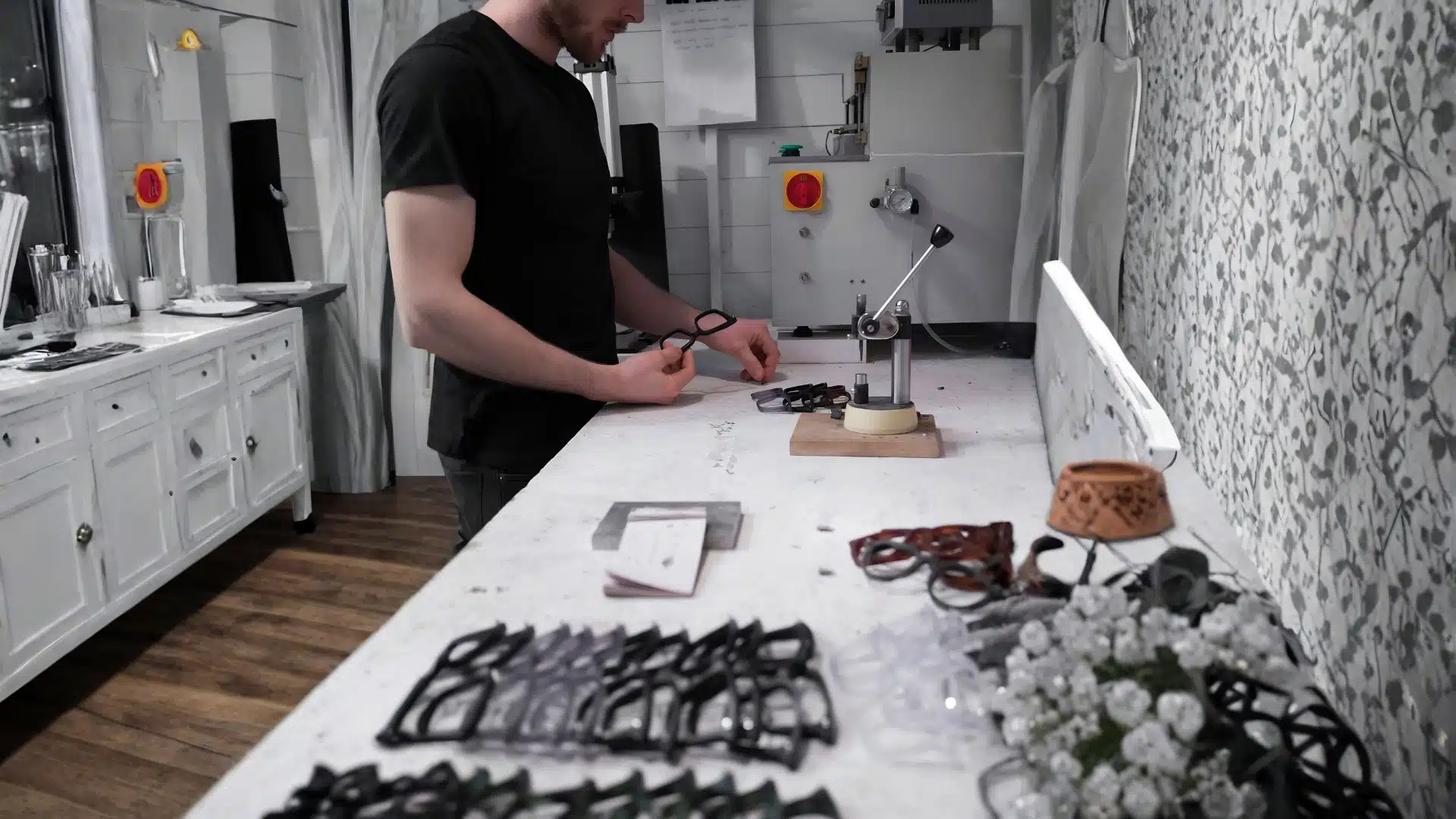 optician adjusting a pair of glasses at a professional workbench surrounded by multiple frames and eyewear tools in a well lit practice