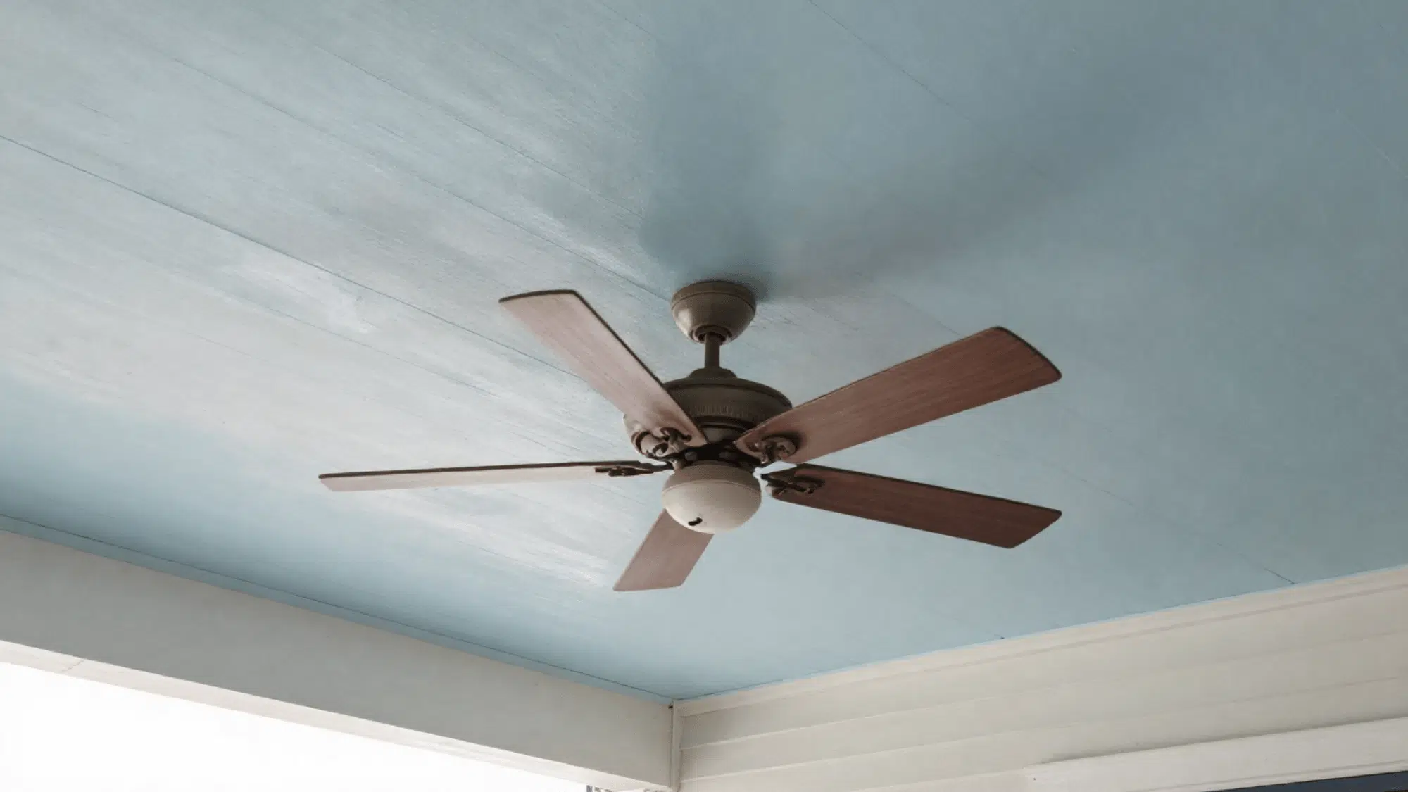 pale blue painted ceiling with a slightly dusty outdoor fan on a covered front porch in natural uneven daylight