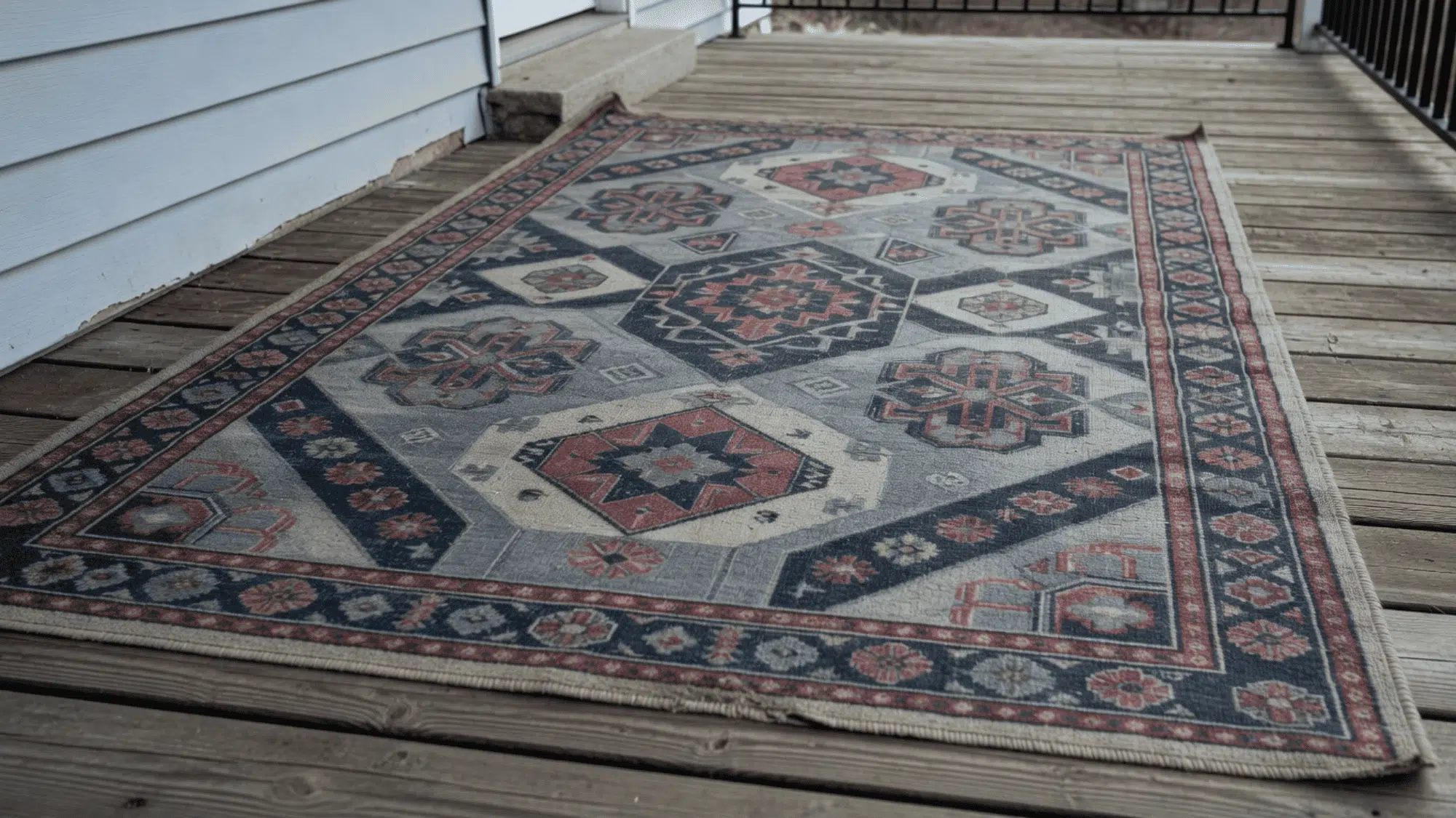 patterned weather resistant area rug on a wooden porch with warped floorboards on a cloudy day in a residential area
