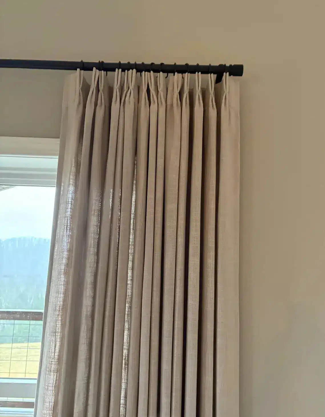 Beige linen curtains hung on a black rod in a sunlit room