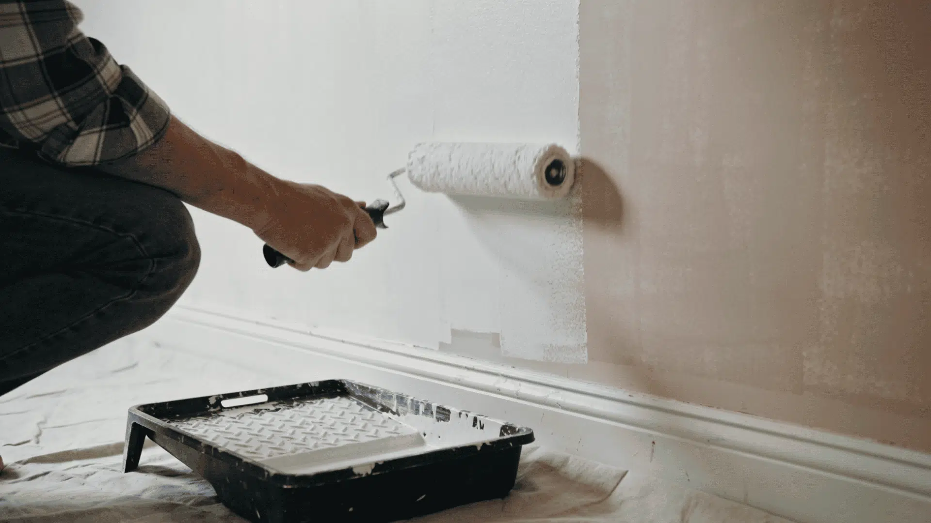 homeowner applying primer to an interior wall with a roller before painting