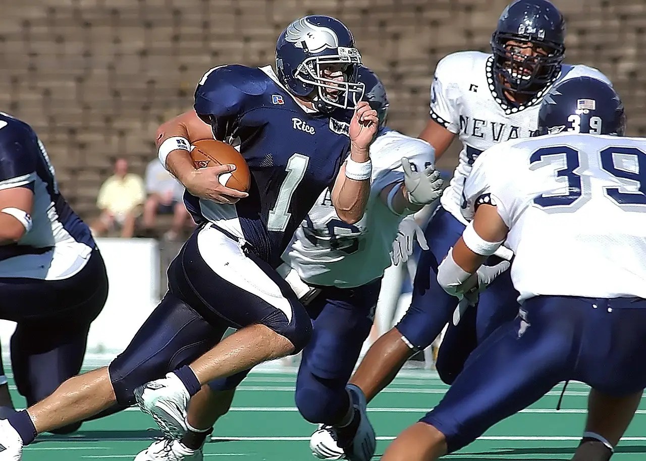 Football player in blue uniform running with ball dodging opponents on field