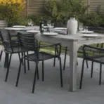 realistic outdoor dining table setup with black chairs on modern patio surrounded by green backyard garden