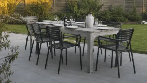 realistic outdoor dining table setup with black chairs on modern patio surrounded by green backyard garden