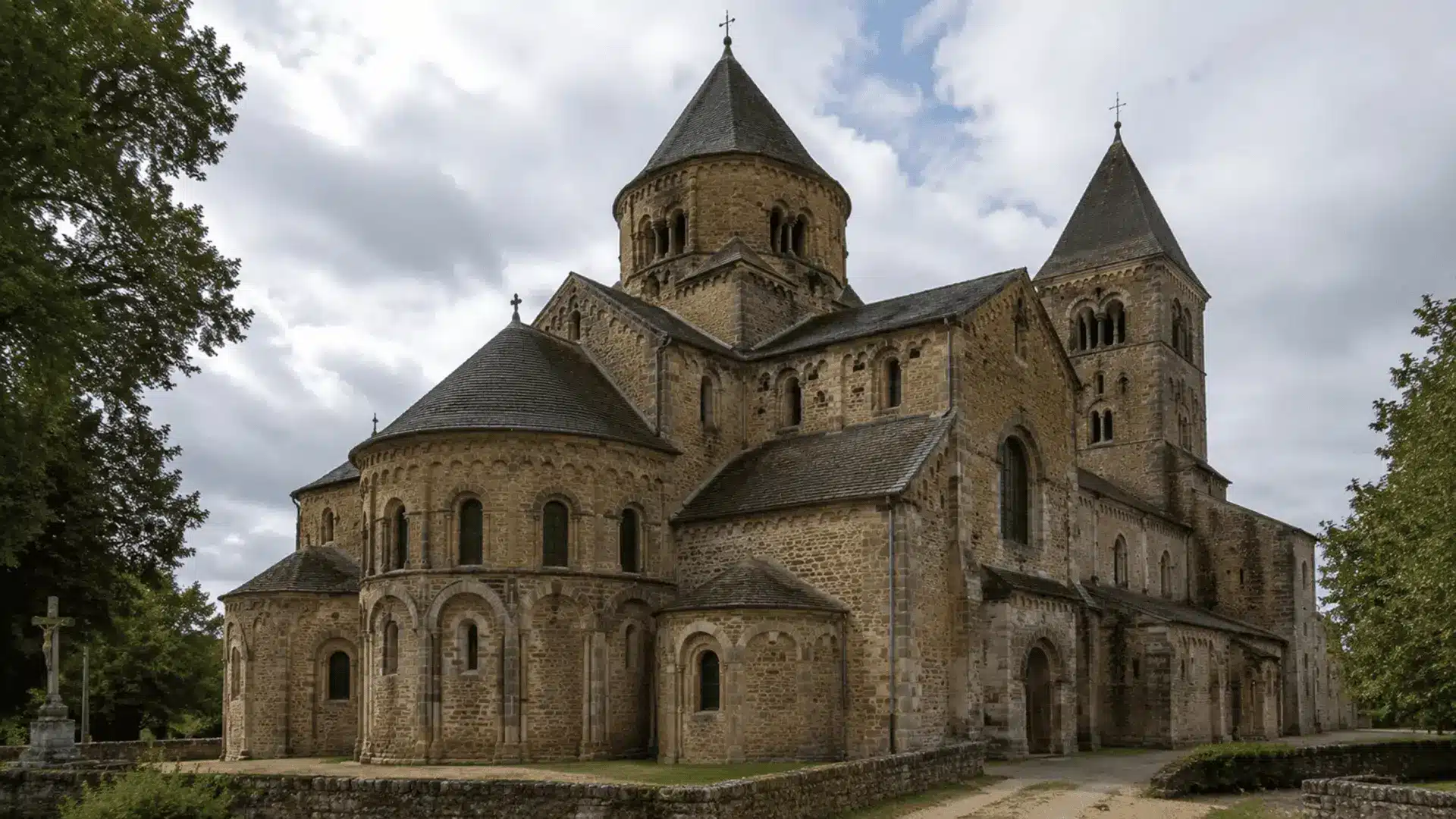 french romanesque church with conical tower roofs and stone apse chapels under a cloudy sky