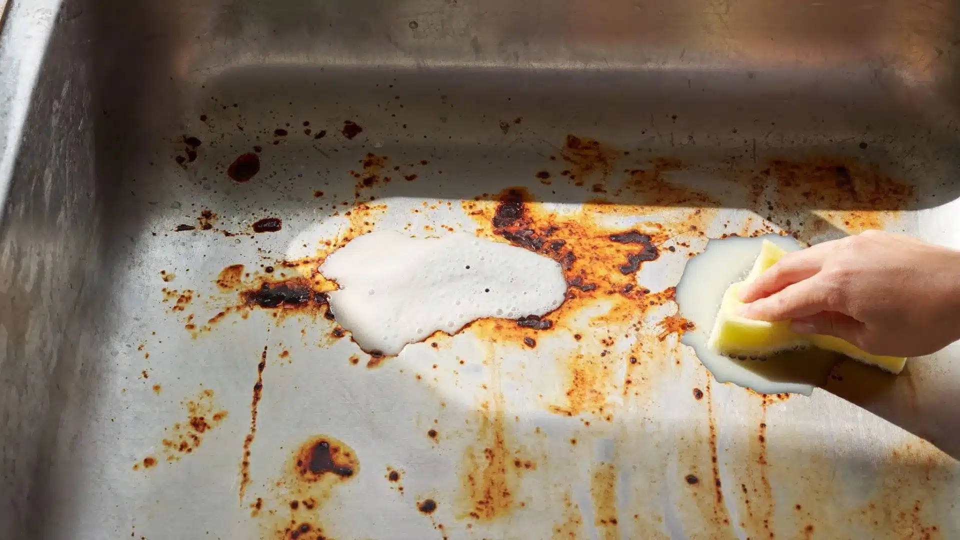 hand using soft sponge with white fizzing paste to clean orange rust stains across stainless steel sink basin