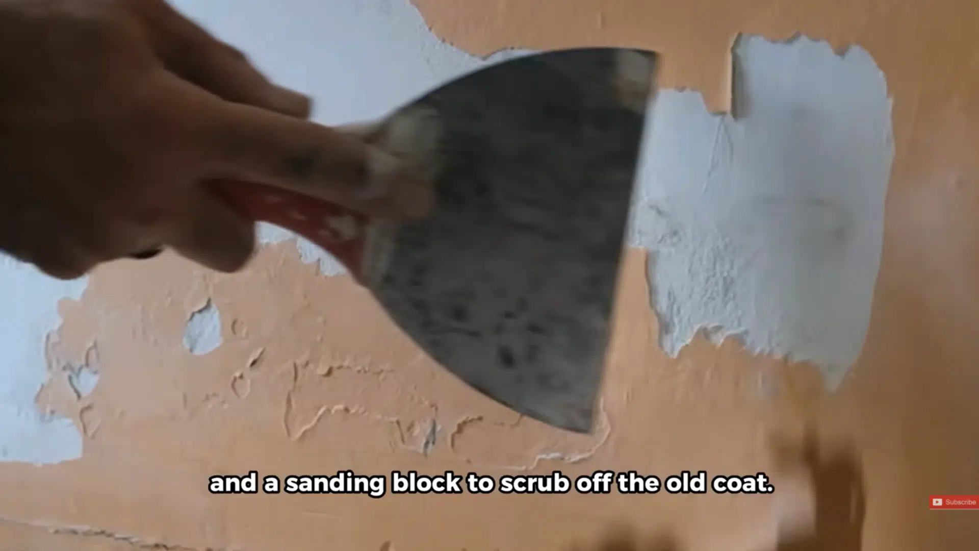 hand using a scraper and sanding block to remove old paint from a rough garage door surface