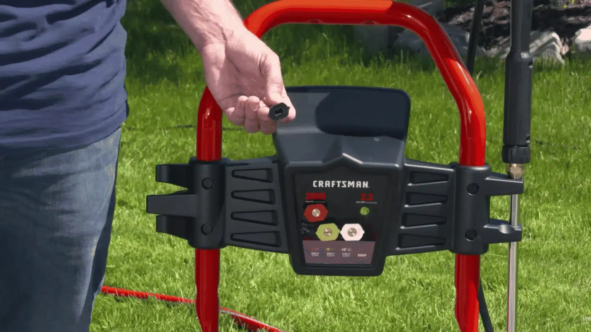 hand installing a spray nozzle tip onto a craftsman pressure washer sitting on a green lawn